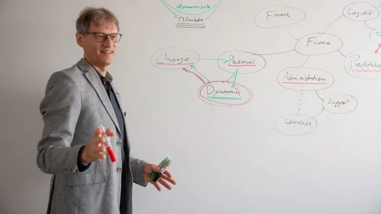 Christian Bracher steht vor einem Mindmap und erklärt erwas